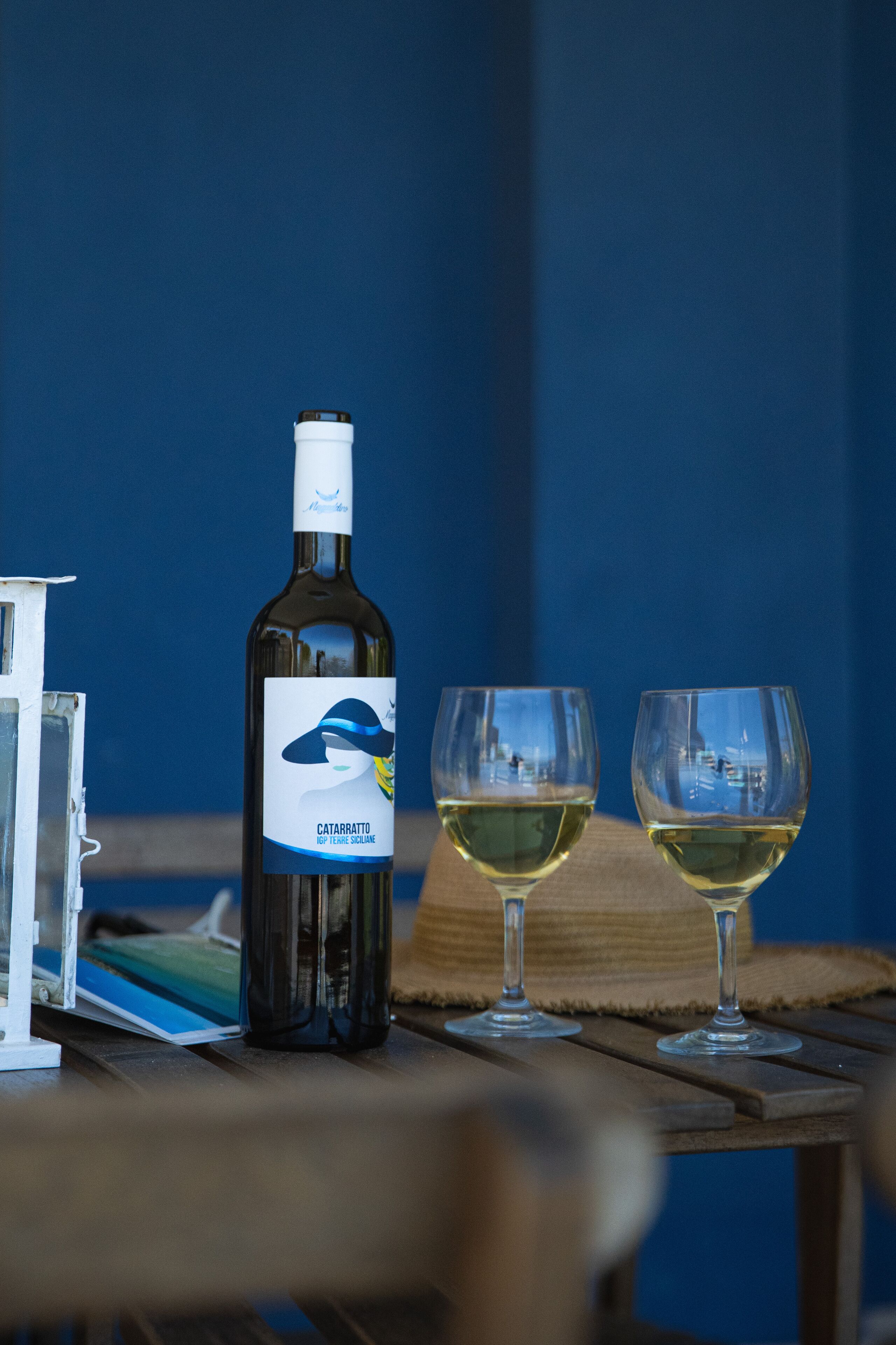 Une bouteille de vin et deux verres sur une table en bois, le tout sur un fond bleu.