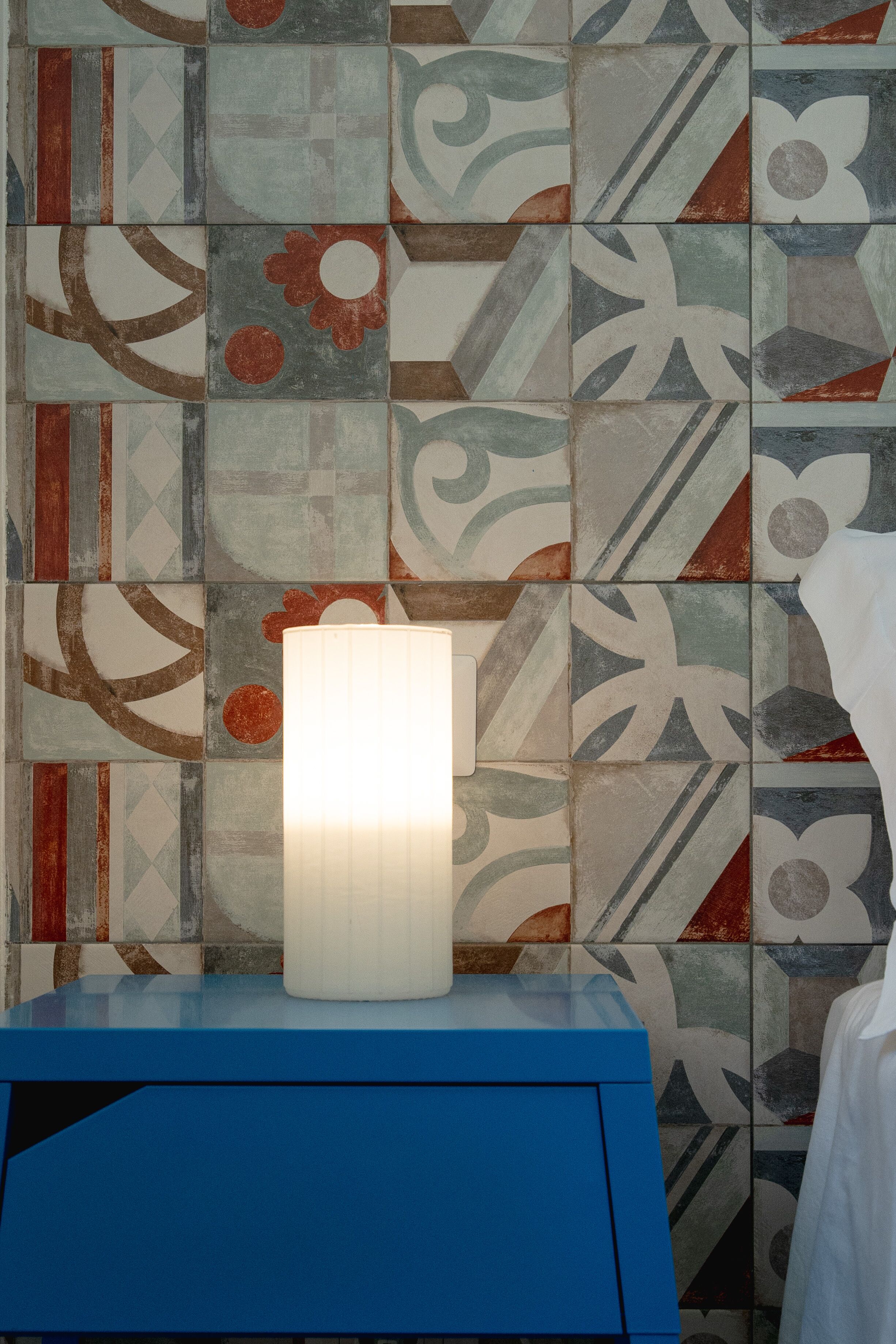 A bathroom with a blue vanity, a white lamp, and a tiled wall with abstract patterns.
