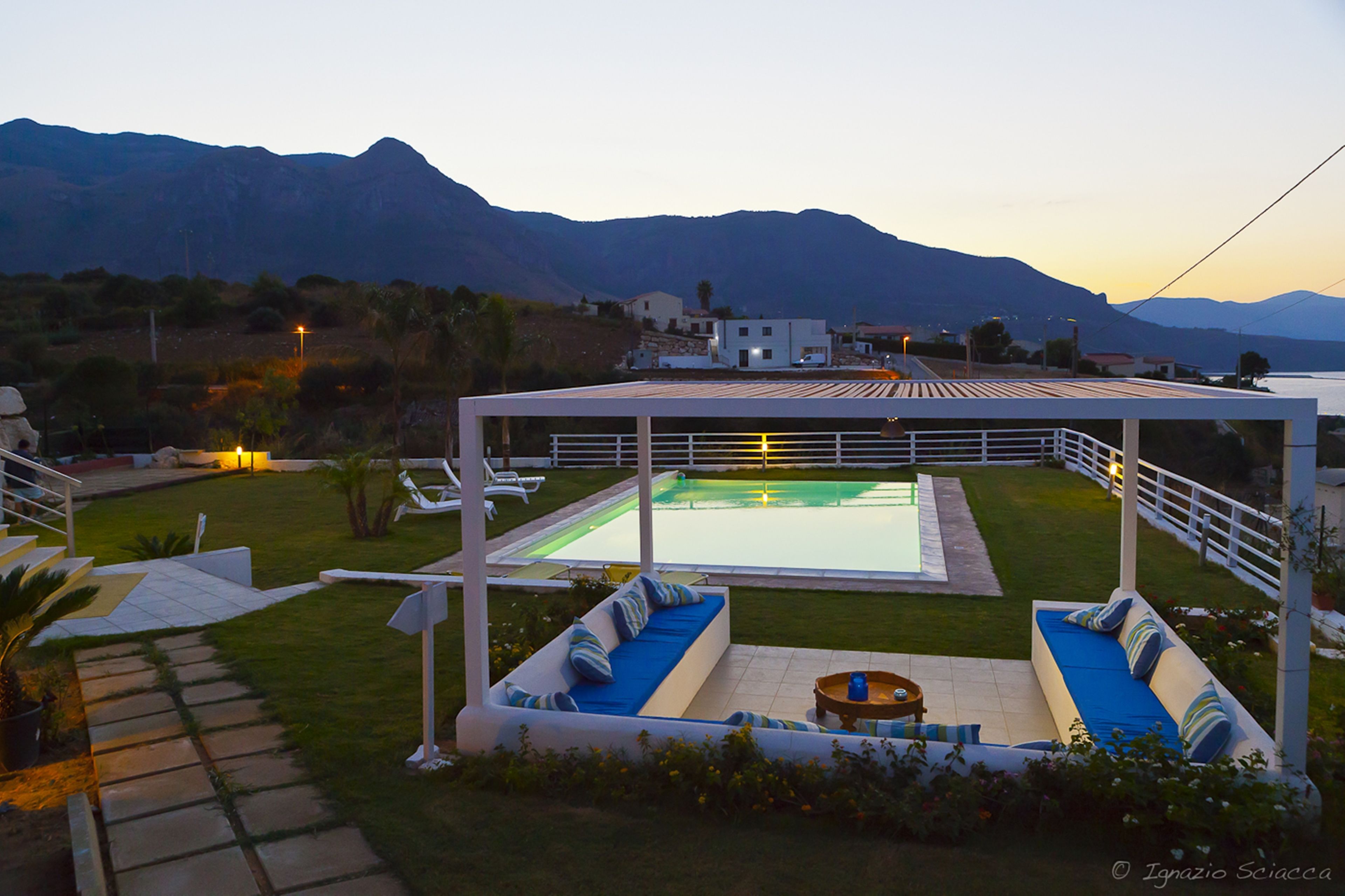 A pool area with a pergola, seating, and a view of mountains.