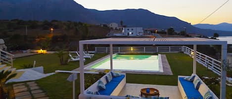 A pool area with a pergola, seating, and a view of mountains.
