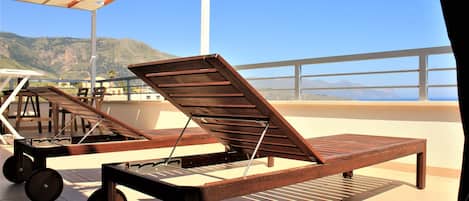 A sun lounger with wheels on a terrace with a view of the sea and mountains.