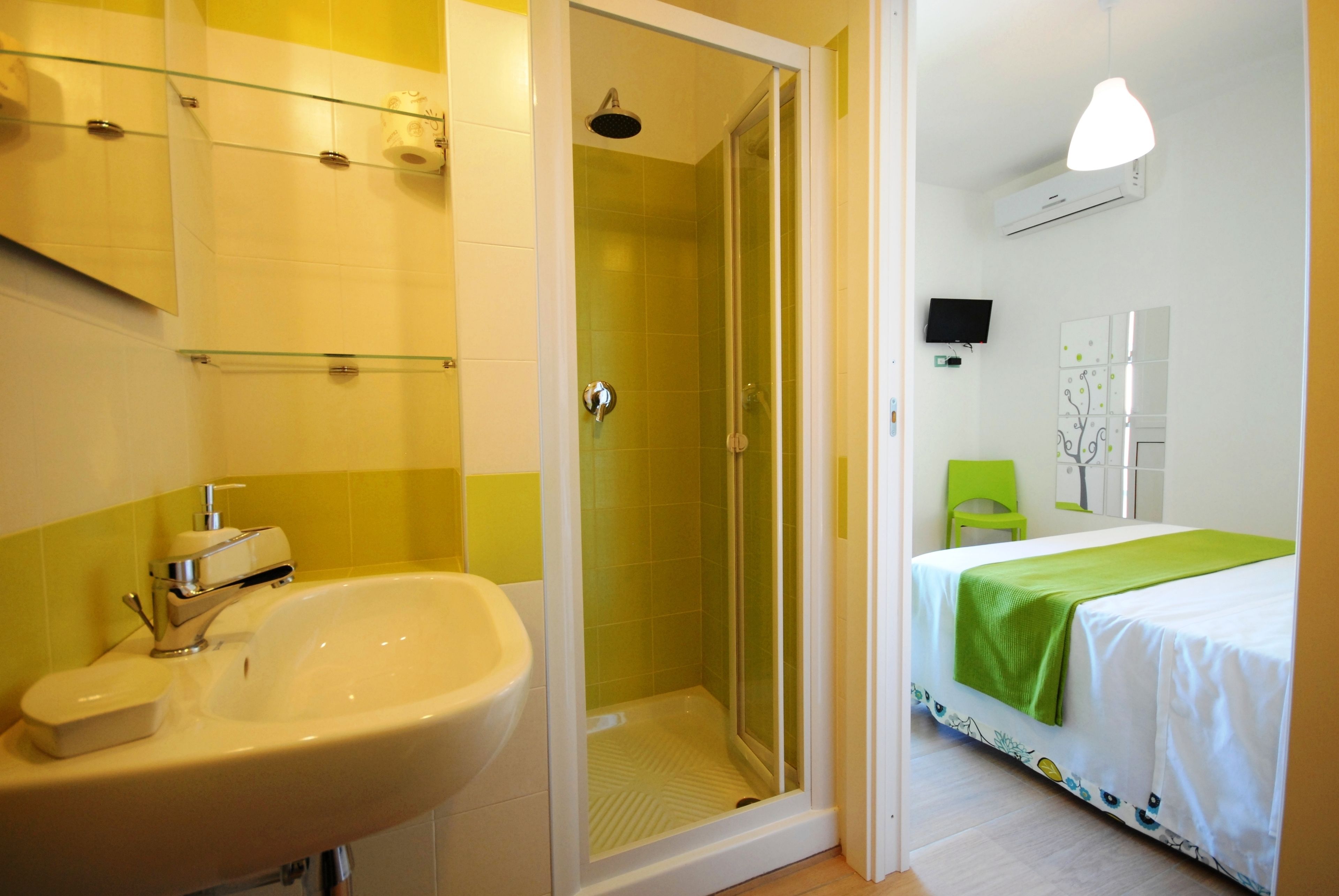 A bathroom with a shower, sink, and a bed with a green bedspread.