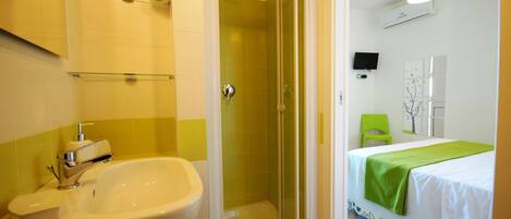 A bathroom with a shower, sink, and a bed with a green bedspread.