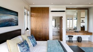A modern bedroom with a large bed, wooden wardrobe, and a bathroom visible through an open door. - Selkirk House (Hermanus)