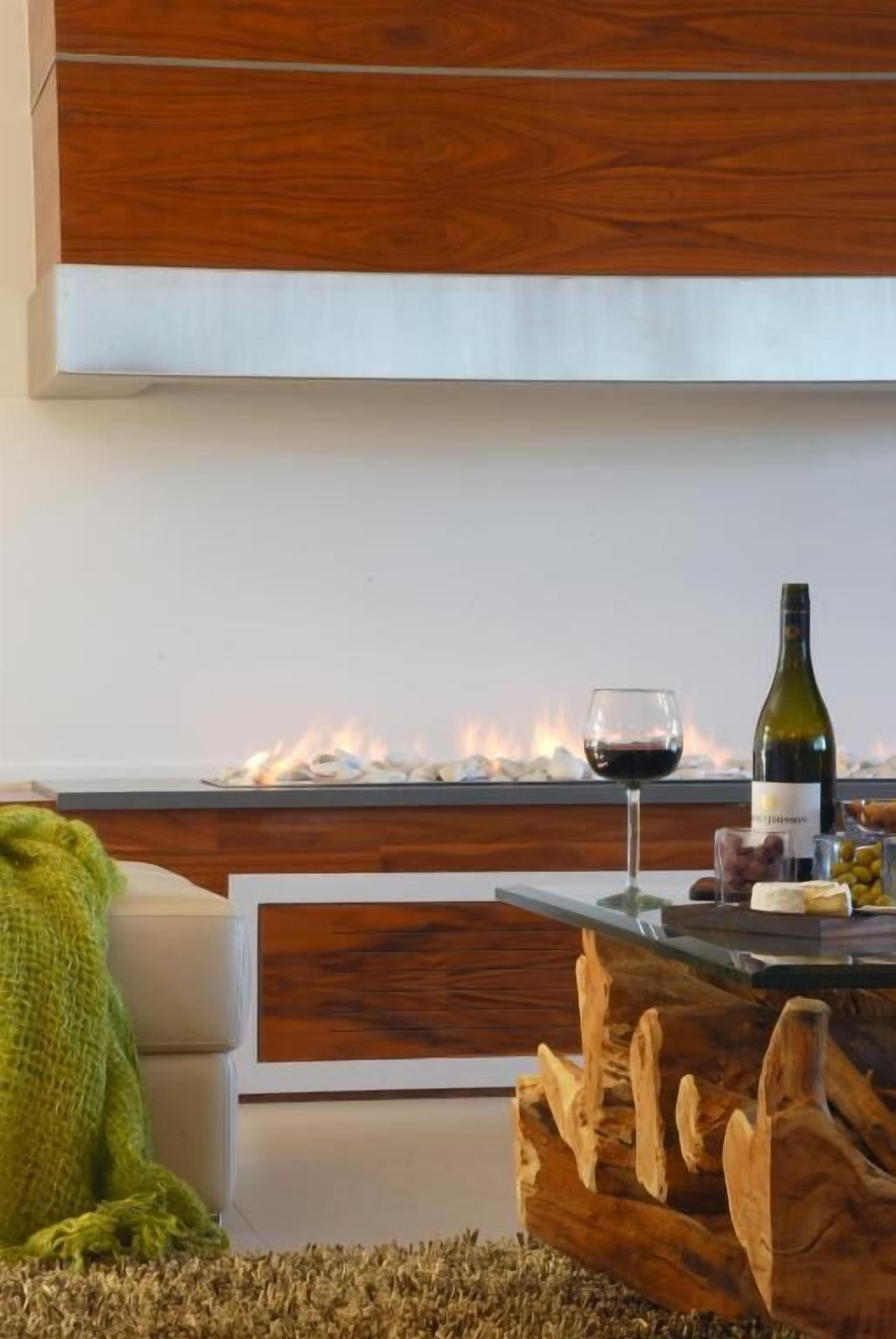 A modern living room with a fireplace, a wooden coffee table, and a green blanket on the floor.