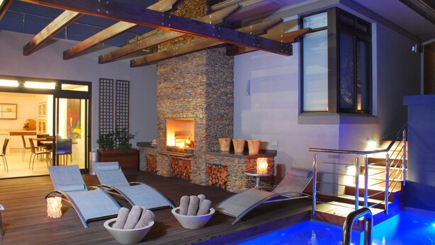 A modern indoor pool area with lounge chairs, a stone fireplace, and a staircase leading to an upper level. - Selkirk House (Hermanus)