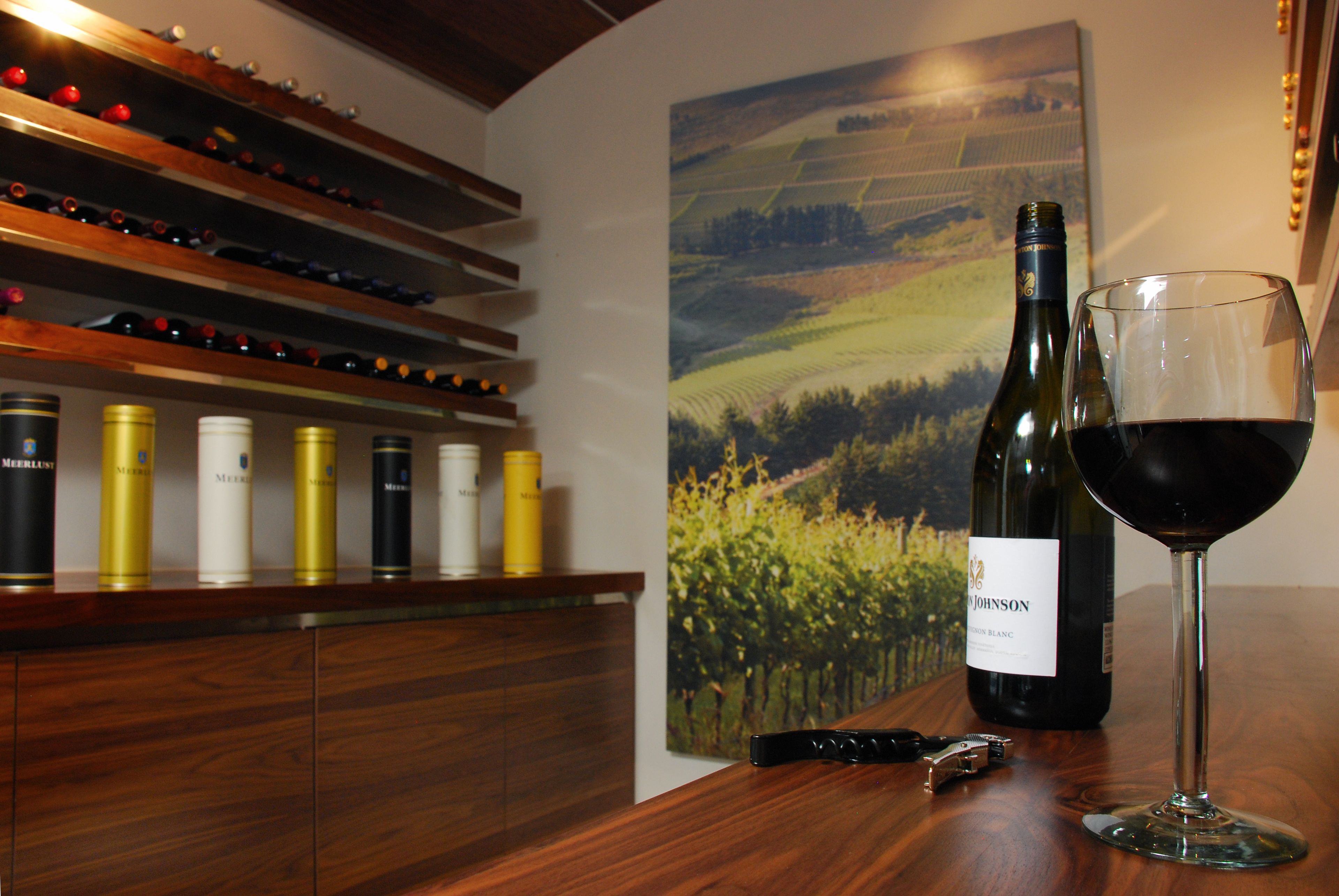 Une bouteille de vin et un verre sur une table en bois, avec un meuble à vin en arrière-plan.