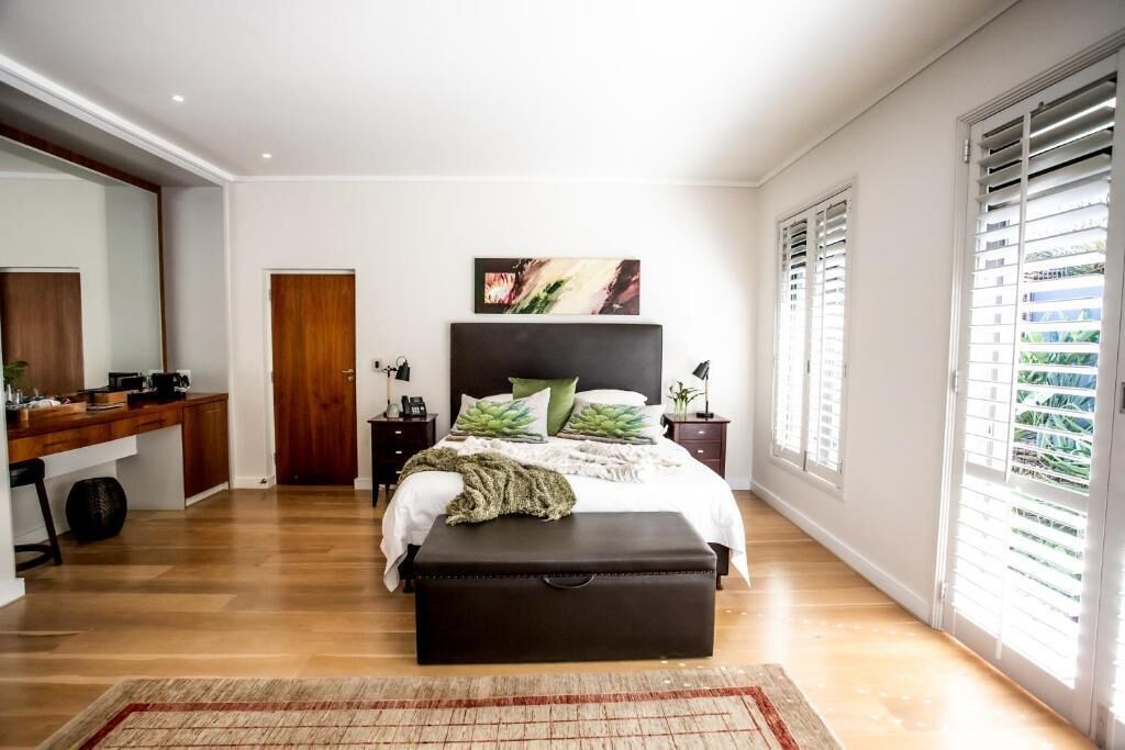 Quarto com cama, cômoda, mesa de cabeceira e janela com persianas.