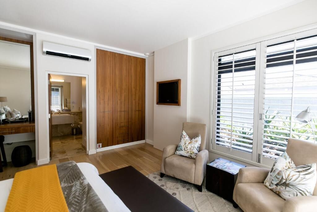 A modern bedroom with a bed, two armchairs, a TV, and a window with blinds.