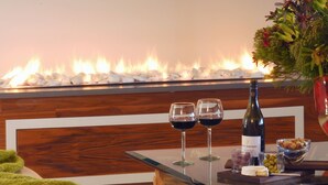A cozy seating area with a fireplace, a glass table with wine glasses, a bottle of wine, and a bowl of snacks. - Selkirk House (Hermanus)