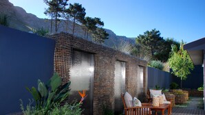 A patio area with a wooden deck, outdoor furniture, and a decorative wall with a cactus plant. - Selkirk House (Hermanus)