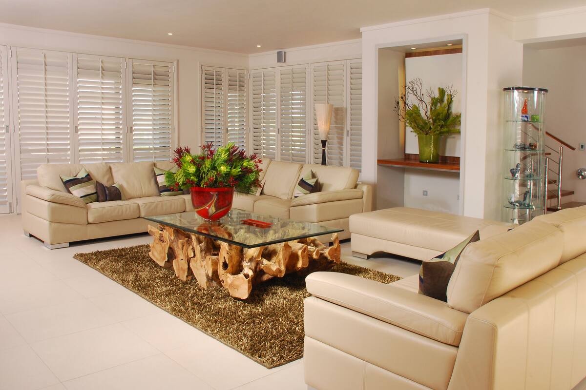 A living room with a glass coffee table, beige sofas, a wooden accent piece, and a decorative plant.