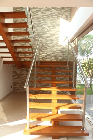 Una escalera moderna con escalones de madera y barandillas de metal, que sube a un piso superior.