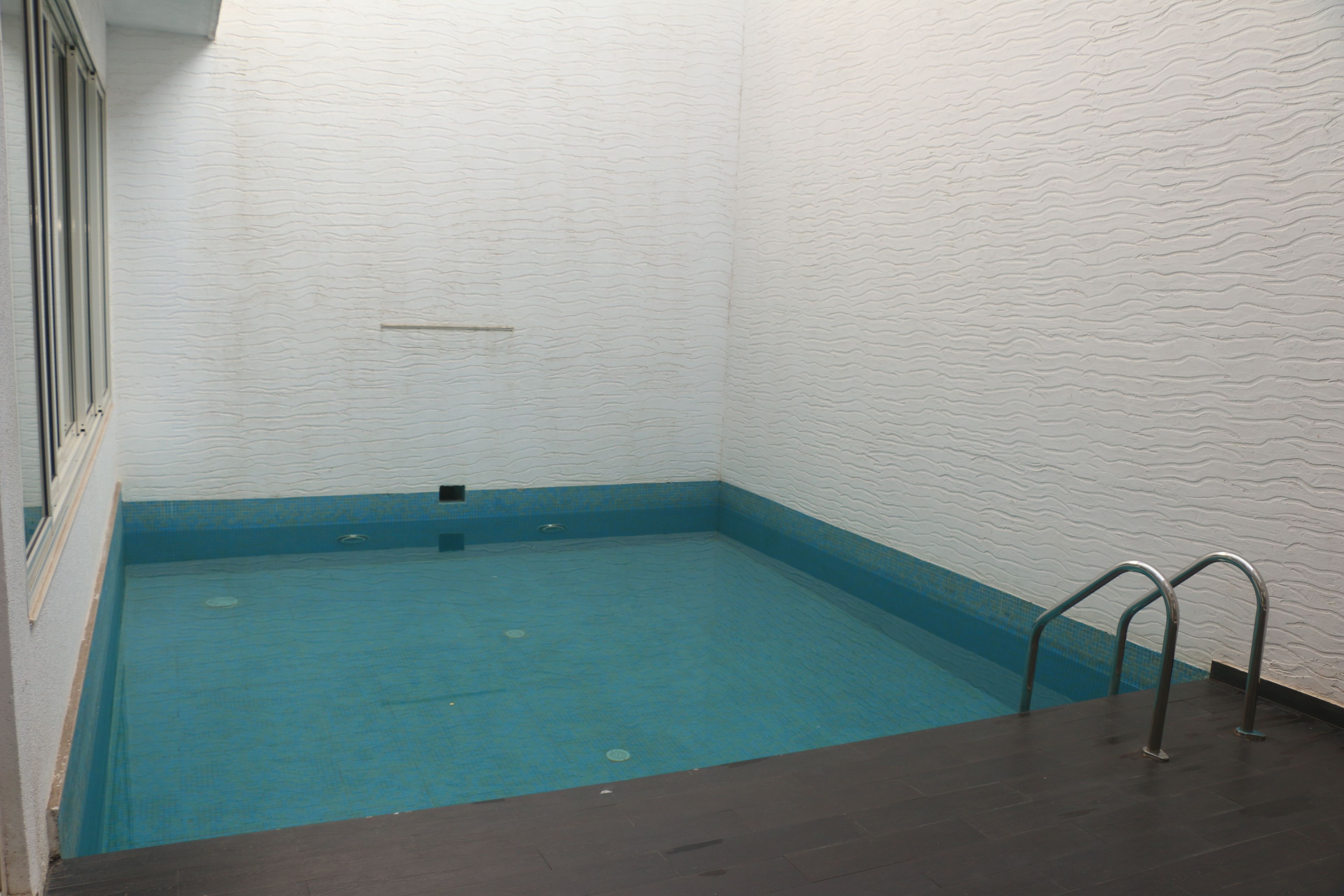 Piscina com interior azul, escada de metal e parede branca texturizada.