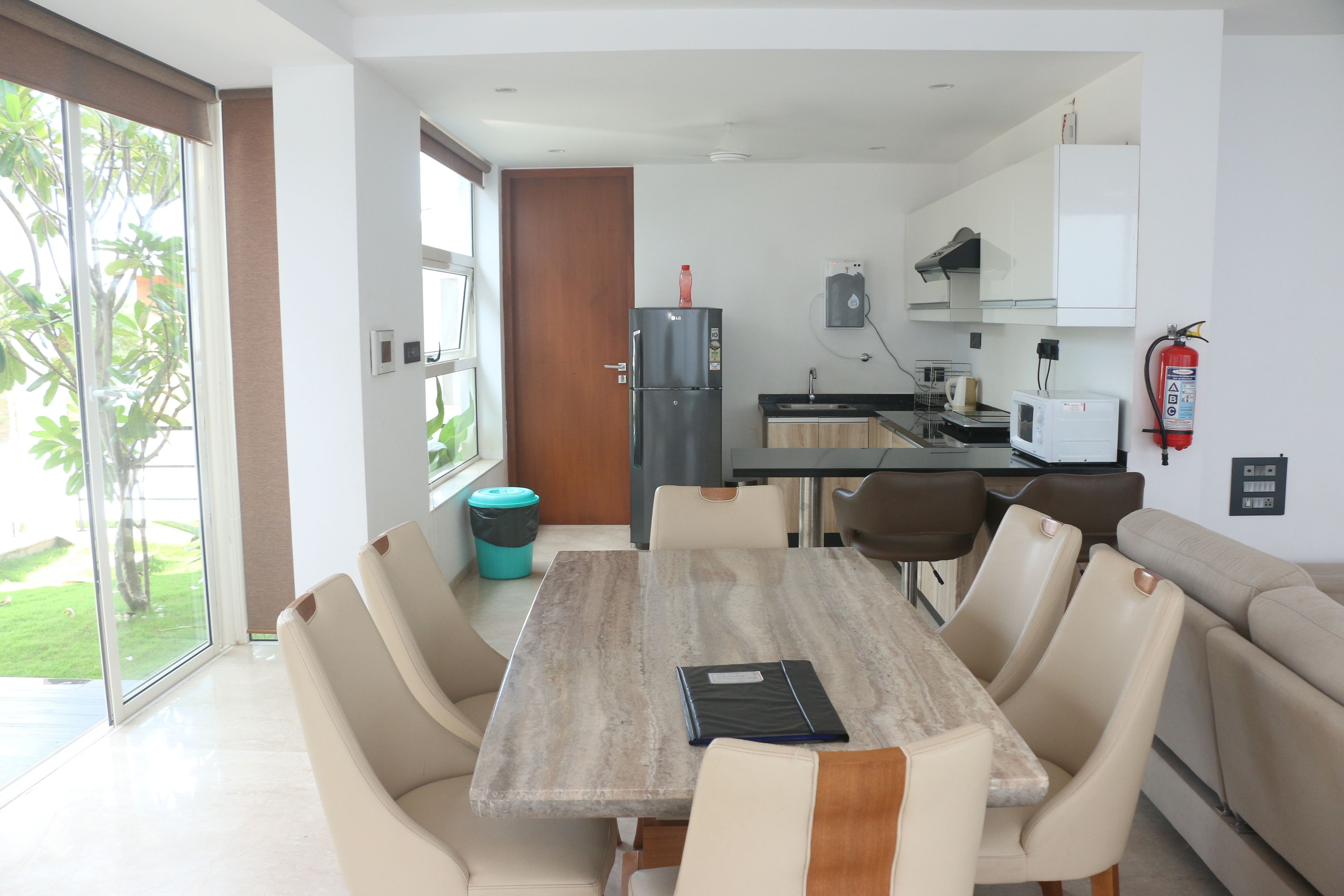 A modern kitchen with a refrigerator, microwave, and sink. There is a dining area with a table and chairs, and a sofa.