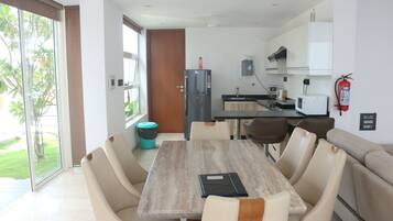 A modern kitchen with a refrigerator, microwave, and sink. There is a dining area with a table and chairs, and a sofa.