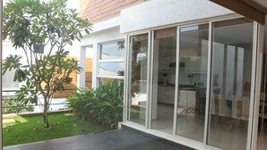Une maison moderne avec une façade en bois, une porte vitrée donnant sur la cuisine et un petit jardin agrémenté d’un arbre et de plantes.