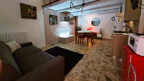 Una sala de estar acogedora con un sofá marrón, un comedor con mesa y sillas, una cocina con un armario rojo y un suelo de piedra.