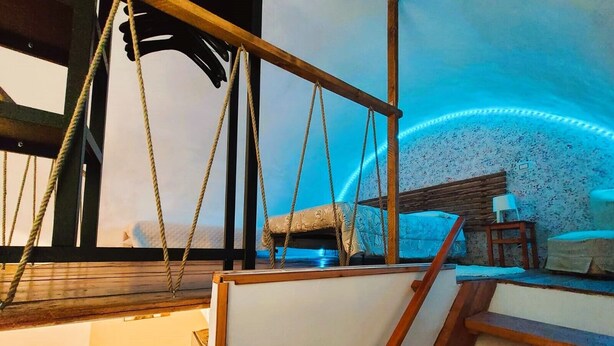 Una habitación con suelo de madera, cama con cubrecama estampado, una mesita con lámpara y pared con diseño floral.