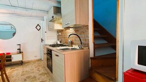 Una cocina compacta con suelo de piedra, un pequeño comedor y un televisor fijado a la pared.