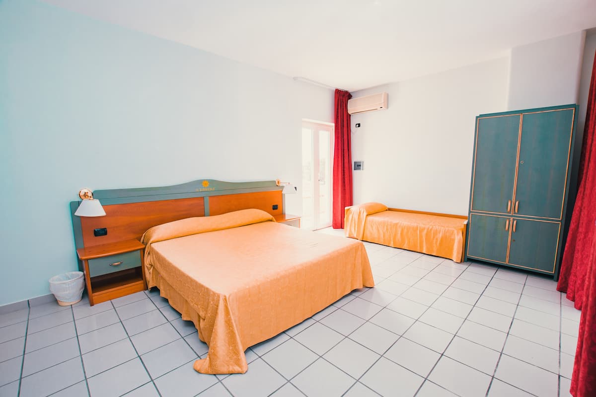 Een hotelkamer met een groot bed, een kleiner bed, een kledingkast, een nachtkastje en een prullenbak.