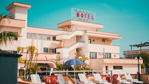 A hotel with a sign reading "HOTEL CLUB" and a terrace with lounge chairs and umbrellas.