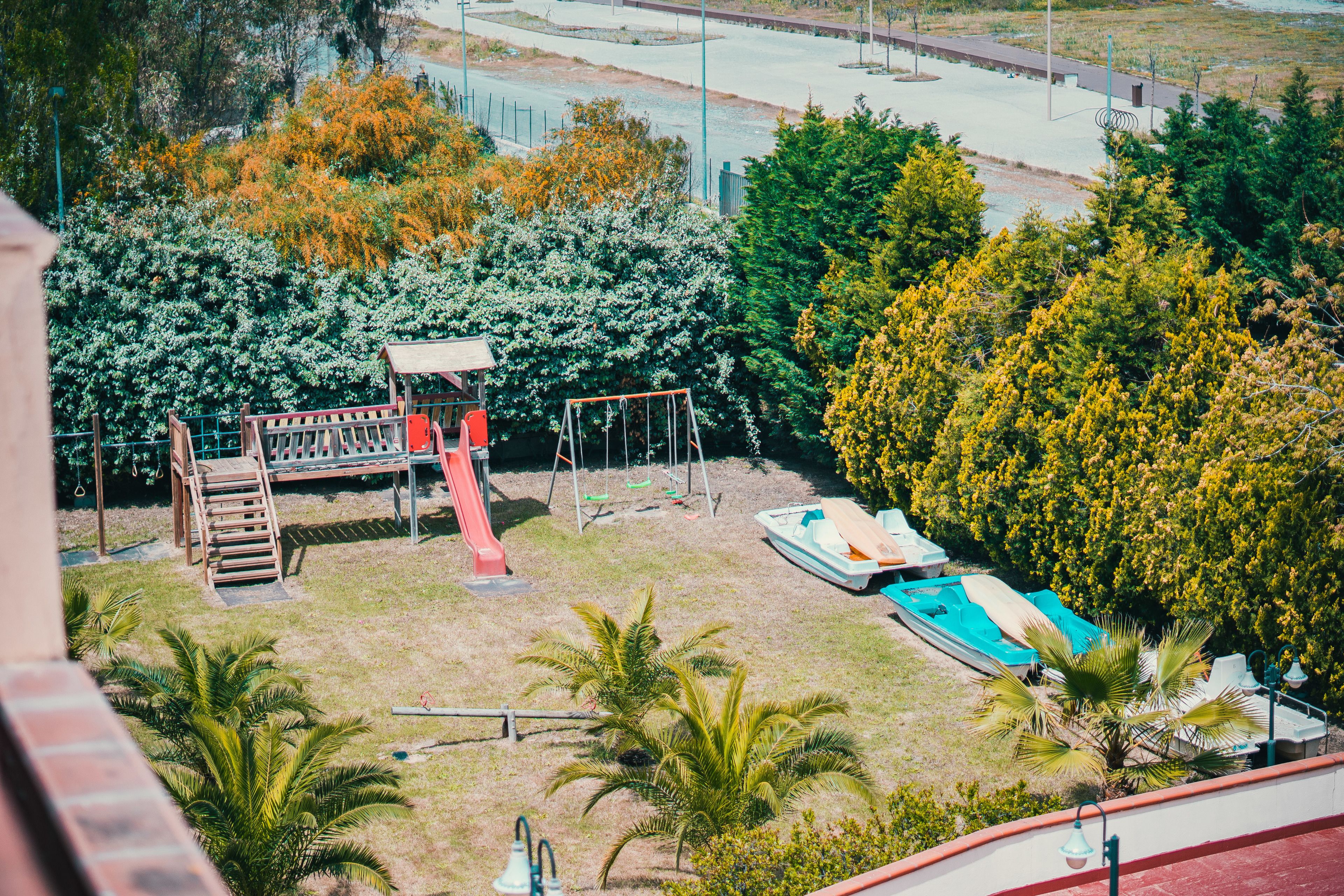 Ein Spielplatz mit Schaukeln und Rutsche, umgeben von Bäumen und einem kleinen Pool.