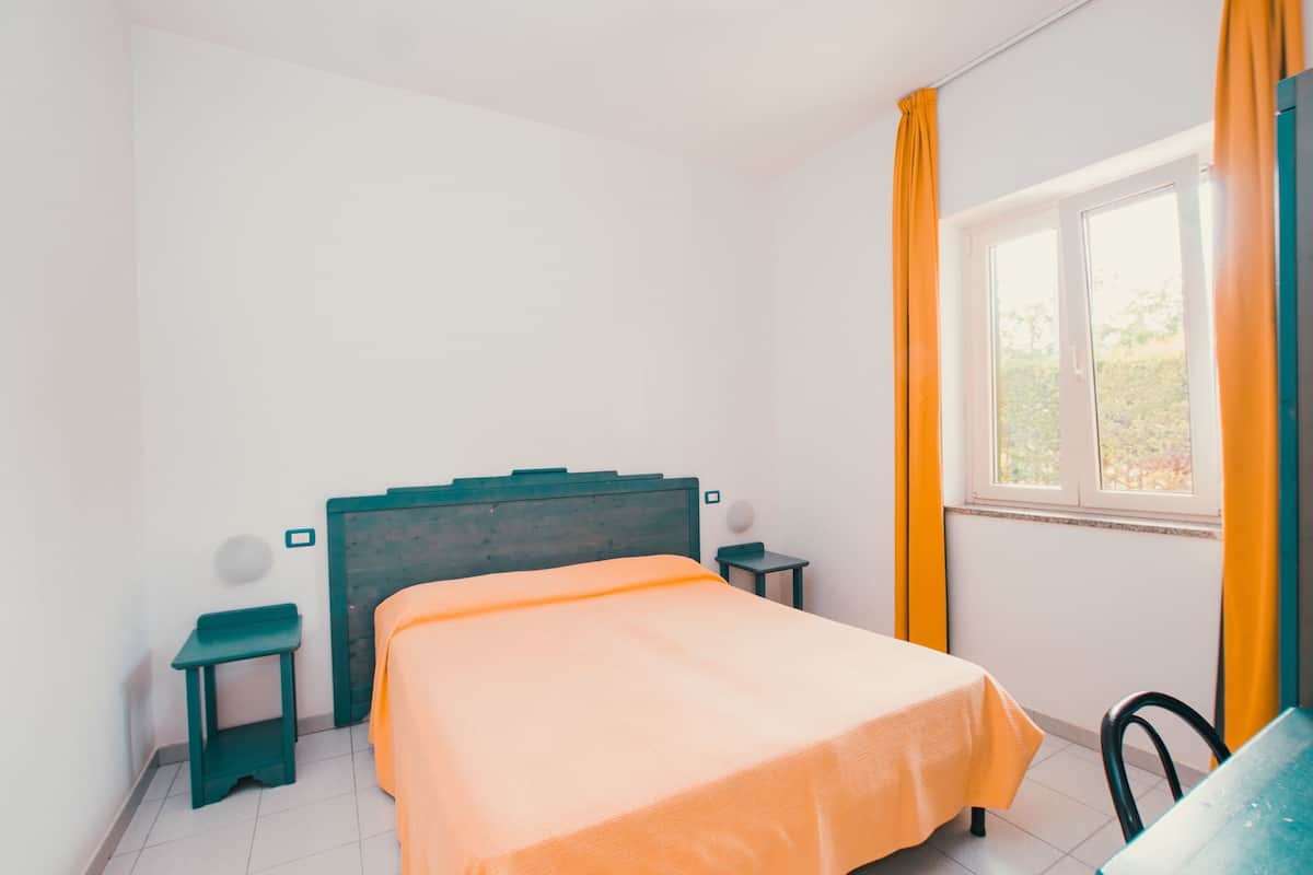 Een slaapkamer met een bed, een nachtkastje, een stoel en een raam met gordijnen.