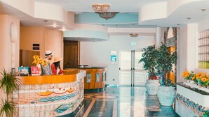 A hotel reception area with a tiled floor, a reception desk, and potted plants.