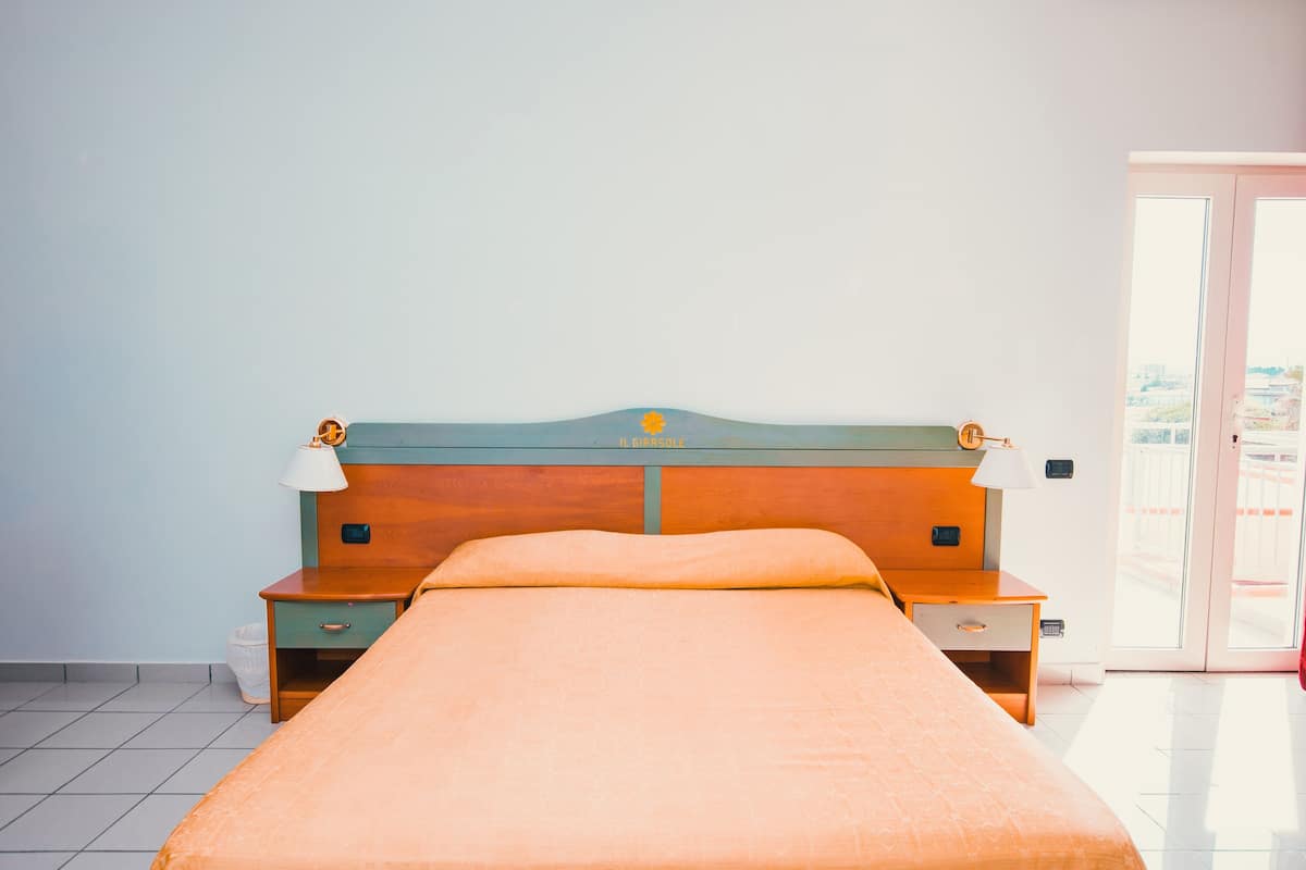 Een eenpersoonskamer met een houten hoofdbord, een nachtkastje en een lamp.