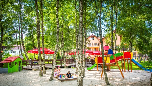 Un parque infantil con arena, árboles y un edificio al fondo.