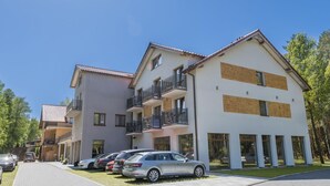 Un edificio residencial de varios pisos con balcones, un camino pavimentado y automóviles estacionados.