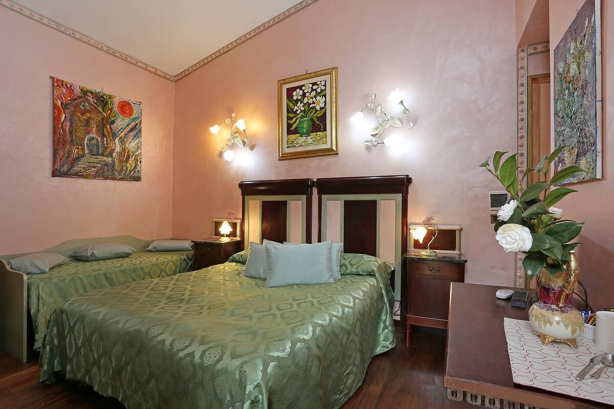 Una habitación de hotel con dos camas, un escritorio, un florero con flores y obras de arte en las paredes.