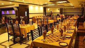A restaurant with multiple tables set with yellow tablecloths and brown chairs. - Hotel Grand Meridian (Katni)