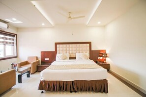 Una habitación de hotel con una cama grande, un escritorio, una silla, una mesita de noche y un ventilador de techo.
