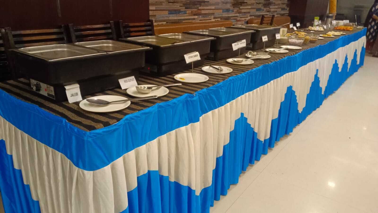 A buffet setup with labeled containers for different food options, a blue and white tablecloth, and a tiled floor.