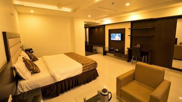 Quarto de hotel com cama, televisão, área de estar e mesa de centro.