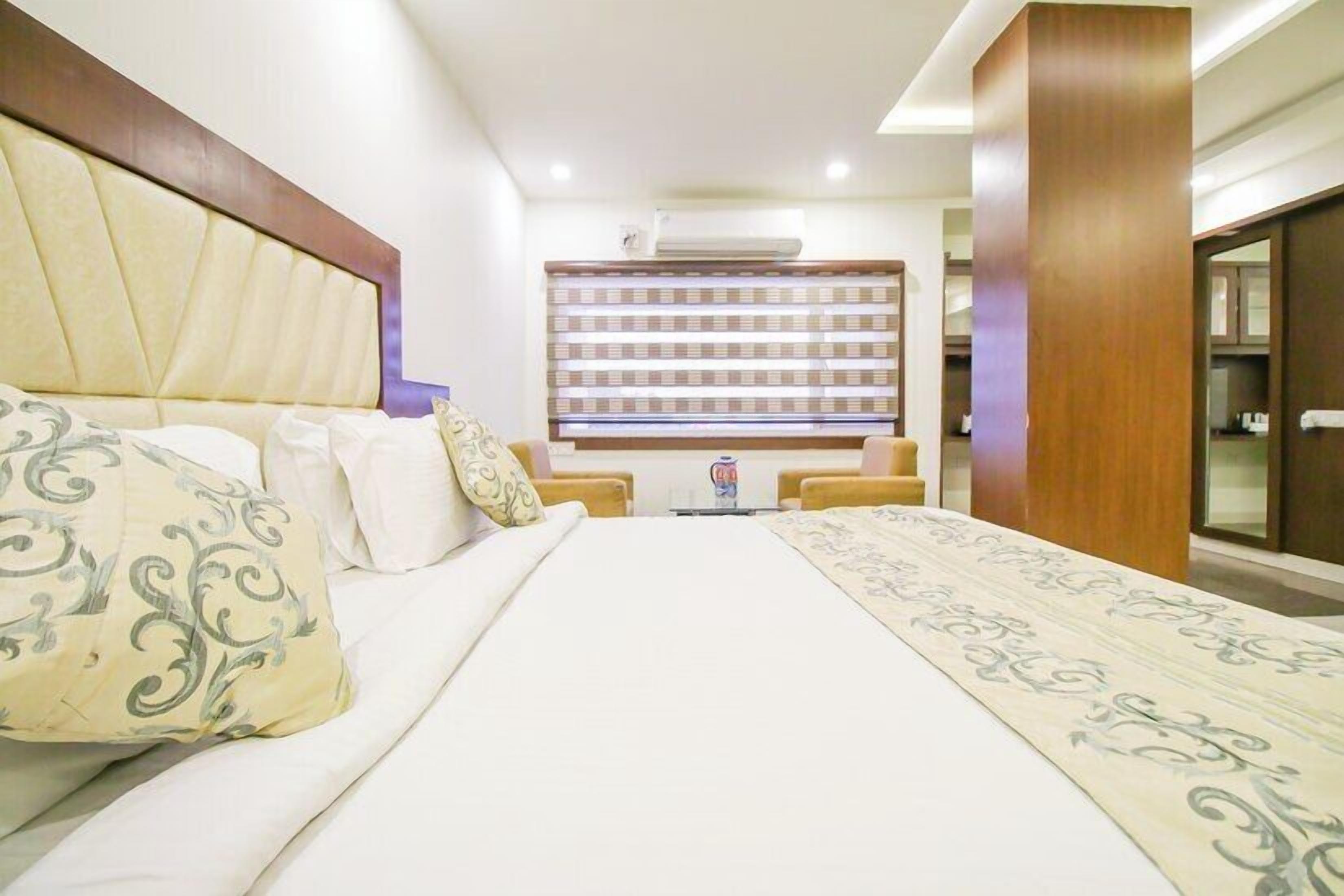 A hotel room with a large bed, a headboard, a minibar, and a wall-mounted shelf with bottles.
