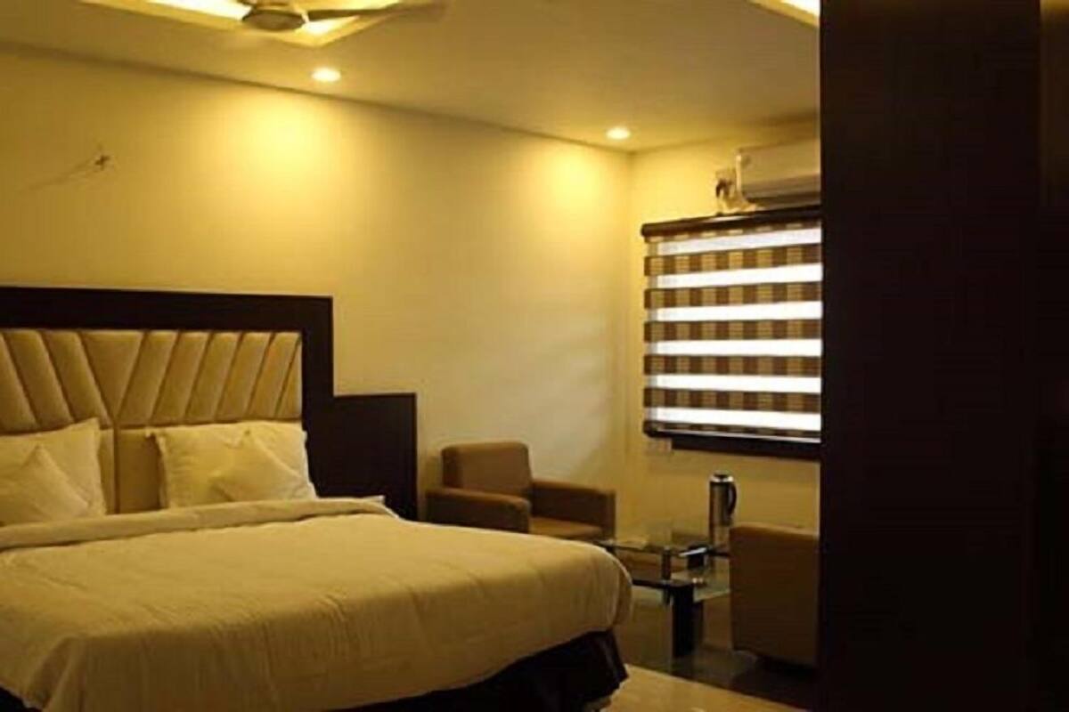 Ein Hotelzimmer mit einem großen Bett, einem Sessel, einem kleinen Tisch und einem Fenster mit Jalousien.