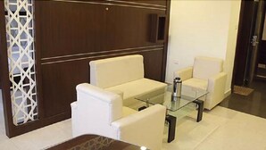 A modern lobby with a white sofa set, a glass coffee table, and a decorative white lattice partition. - Hotel Grand Meridian (Katni)