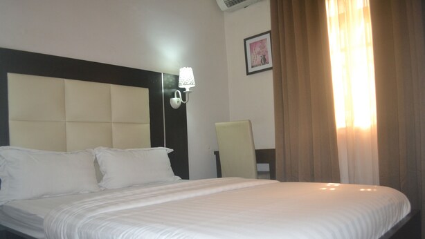 A hotel room with a large bed, a nightstand, a wall-mounted lamp, and a framed picture on the wall. - Mac Dove Lounge & Suites ltd (Lagos)