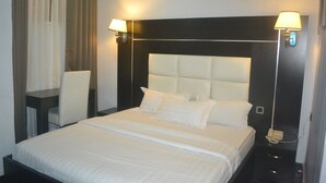 A hotel room with a large bed, two bedside lamps, a desk, and a chair. - Mac Dove Lounge & Suites ltd (Lagos)