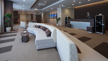 A modern hotel lobby with a reception desk, a large curved sofa, a small side table, and a potted plant.