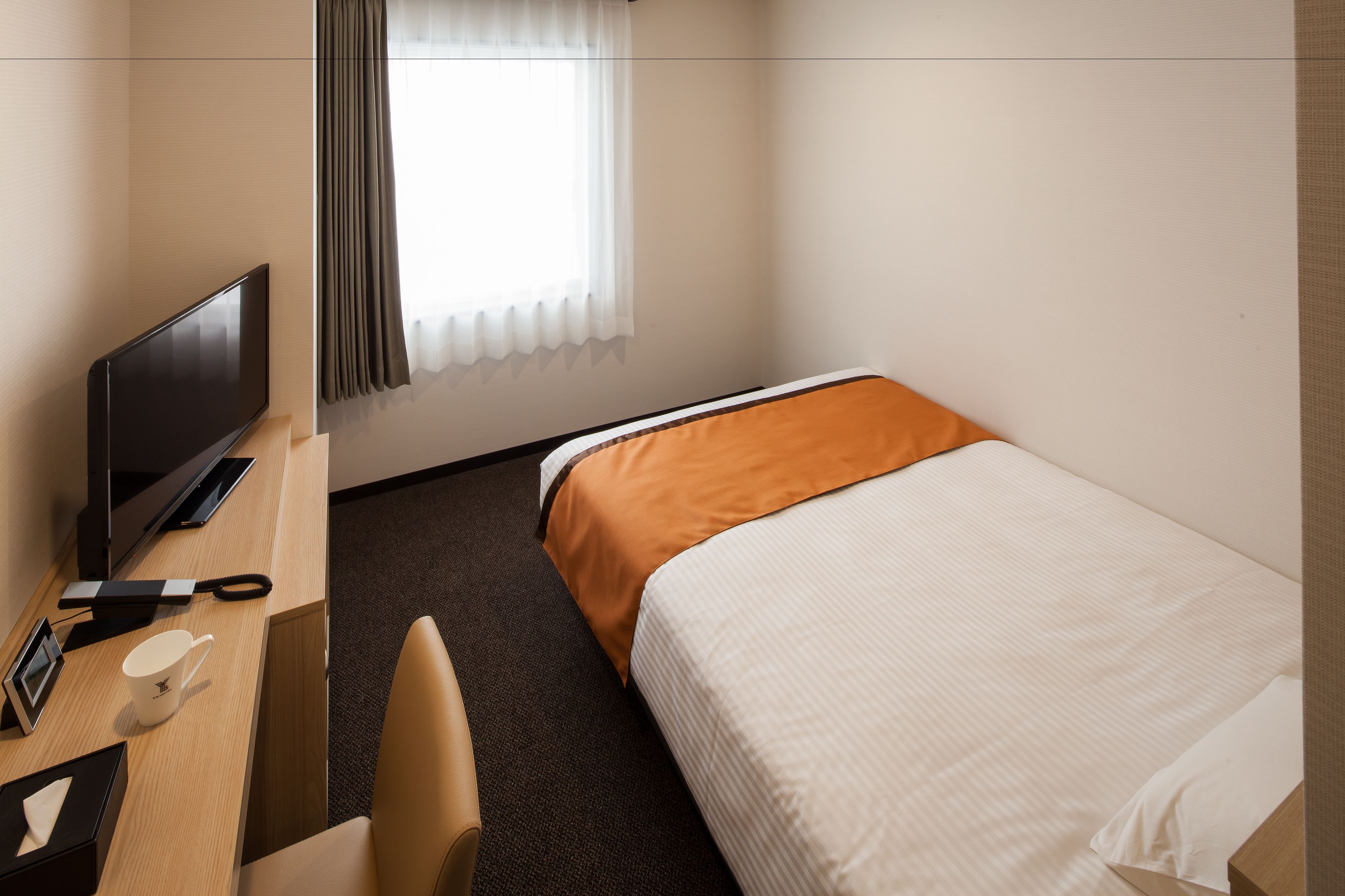 Een hotelkamer met een bed, een bureau met een televisie, een stoel en een raam met gordijnen.