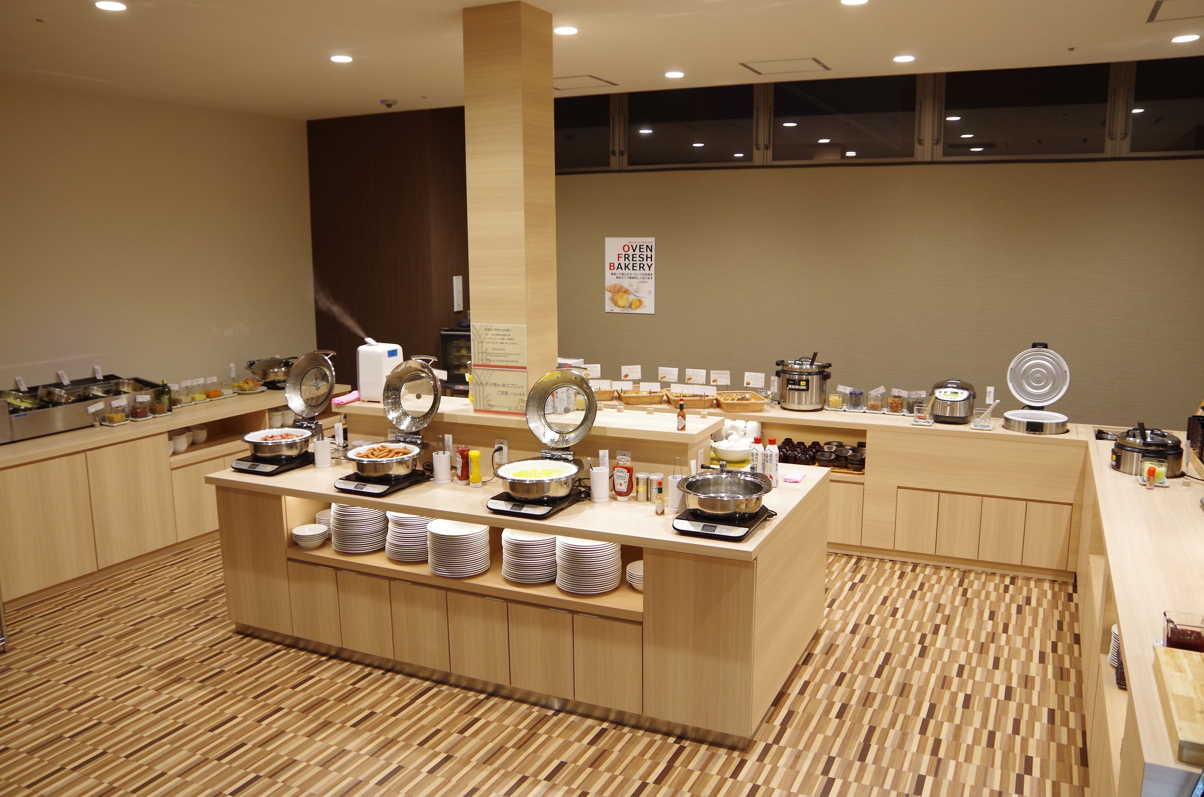 Un buffet proposant une variété de plats et d’accompagnements, un panneau indiquant une boulangerie où les produits sont préparés sur place et un sol carrelé.