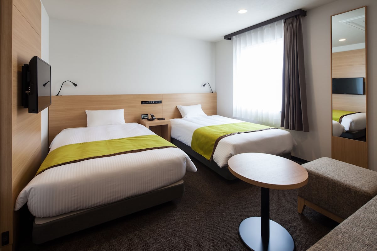 Habitación de hotel con dos camas, una mesita redonda, televisor y espejo.