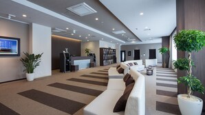 A modern hotel lobby with a reception desk, seating area, and potted plants.