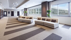 A spacious lobby with two sofas, a patterned carpet, and large windows offering views of the outside.