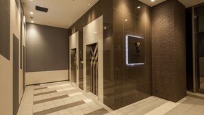A modern hallway with a checkered floor, a wall-mounted light, and a door with a geometric design.
