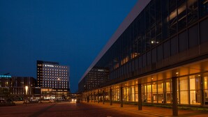 A modern hotel with a glass facade, a spacious lobby, and a parking area.